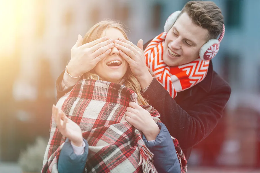 Мъж, който закрива очите на жена с ръка, докато й прави изненадващ подарък